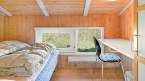 Een kamer met een bed, bureau en stoel, met houten wanden en een raam.