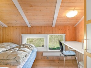 A room with a bed, a desk, and a chair, with wooden walls and a window.