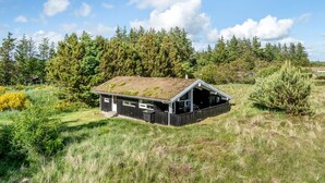 Een blokhut met een schuin dak, omringd door dicht bos en grasland.