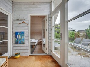 A room with a bed, a painting, a hanging coat rack, and a view of the outside.