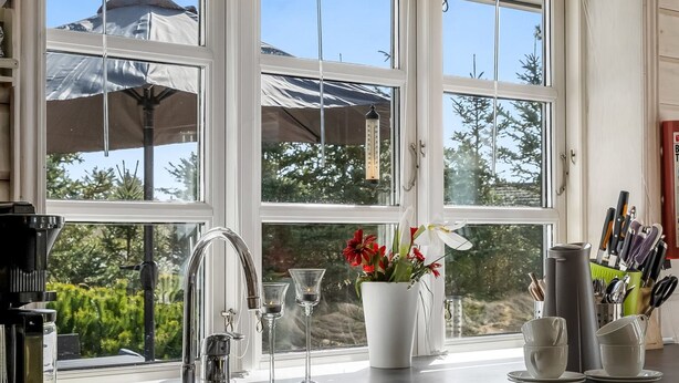 A kitchen with a sink, a coffee machine, and a window with a view of trees and a house.