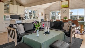 A cozy, open-plan living area with a sofa set, a dining table, and a kitchen in the background.