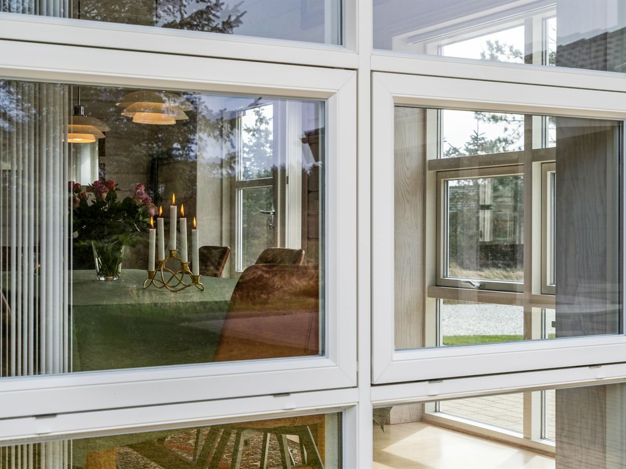 A modern interior with large windows, a dining area with a table and chairs, and a decorative candle holder.