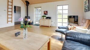 En rummelig stue med et træbord, en sort lædersofa og et fjernsyn. Der er en pejs, en stige og et billede på væggen.