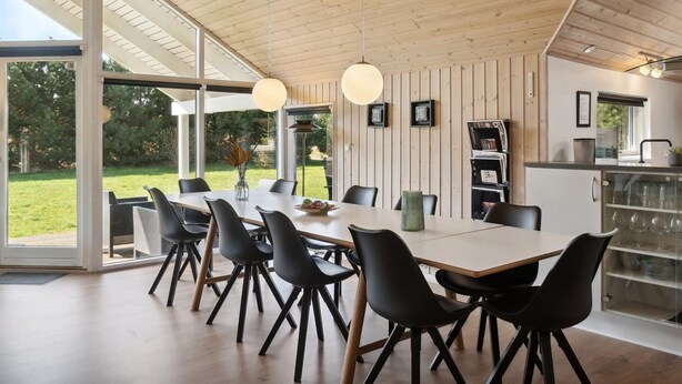 Un espace repas moderne avec une grande table, des chaises noires et une vue sur l’extérieur.