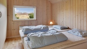 Une pièce aux murs en bois, une fenêtre donnant sur un paysage agréable, deux lits avec des oreillers, une table avec une lampe et un radiateur.