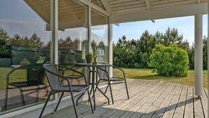 Un espace extérieur abrité, doté d’une terrasse en bois, de chaises en métal, d’une table et d’une plante en pot.