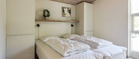 Une chambre à coucher avec un lit, un plafond en bois, des murs blancs, une fenêtre et un tableau accroché au mur.