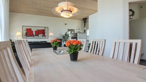 Een eetgedeelte met een lange tafel, witte stoelen en potten met oranje bloemen.