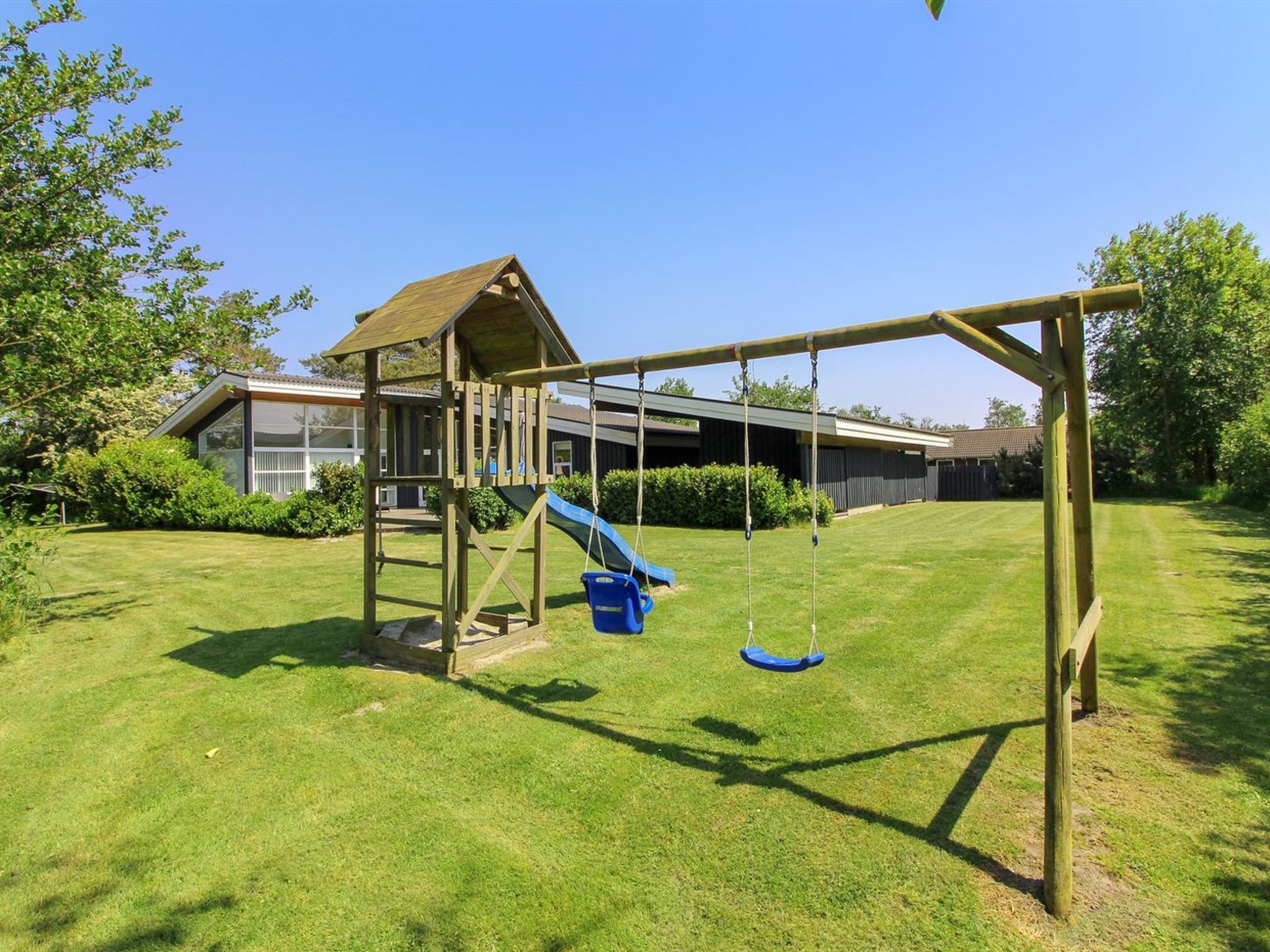 A wooden swing set with a slide in a backyard.