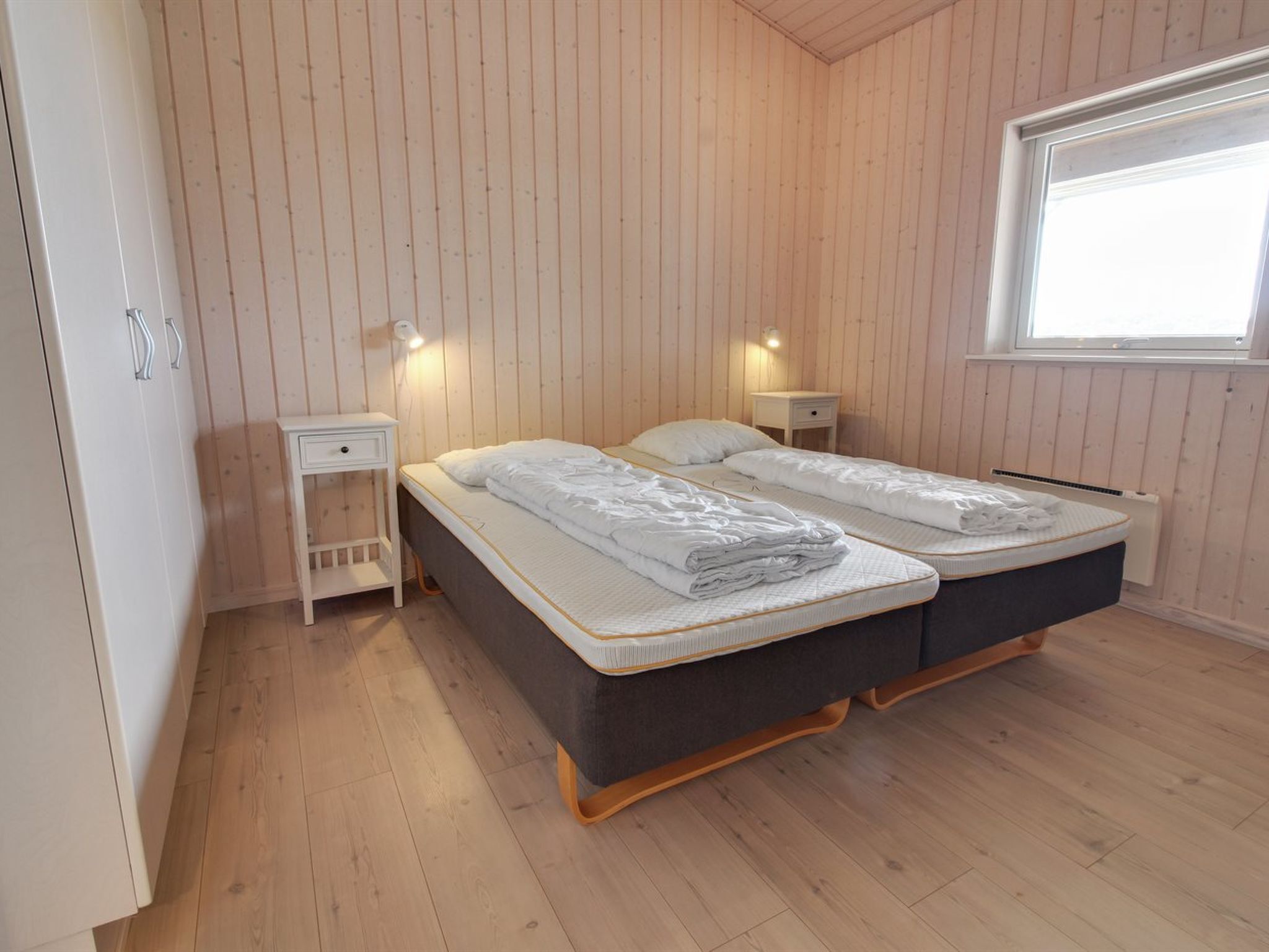 Une chambre avec deux lits, des murs en bois, une fenêtre et des lampes de chevet.