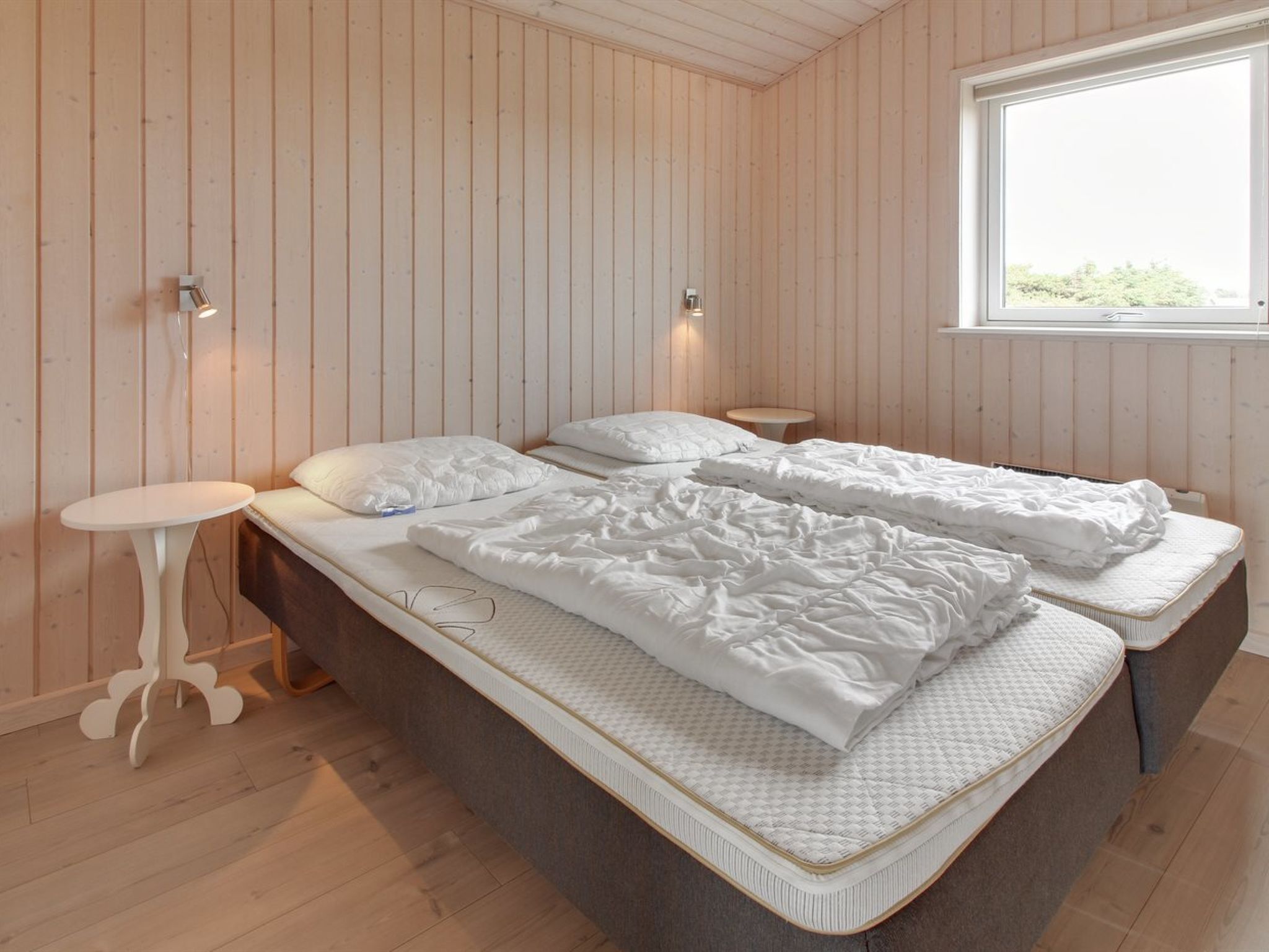 A bedroom with two beds, wooden walls, a small round table, and a window.