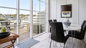 Comedor moderno con vistas a un puerto deportivo, que incluye una mesa redonda, sillas negras, un cuenco y una lámpara.