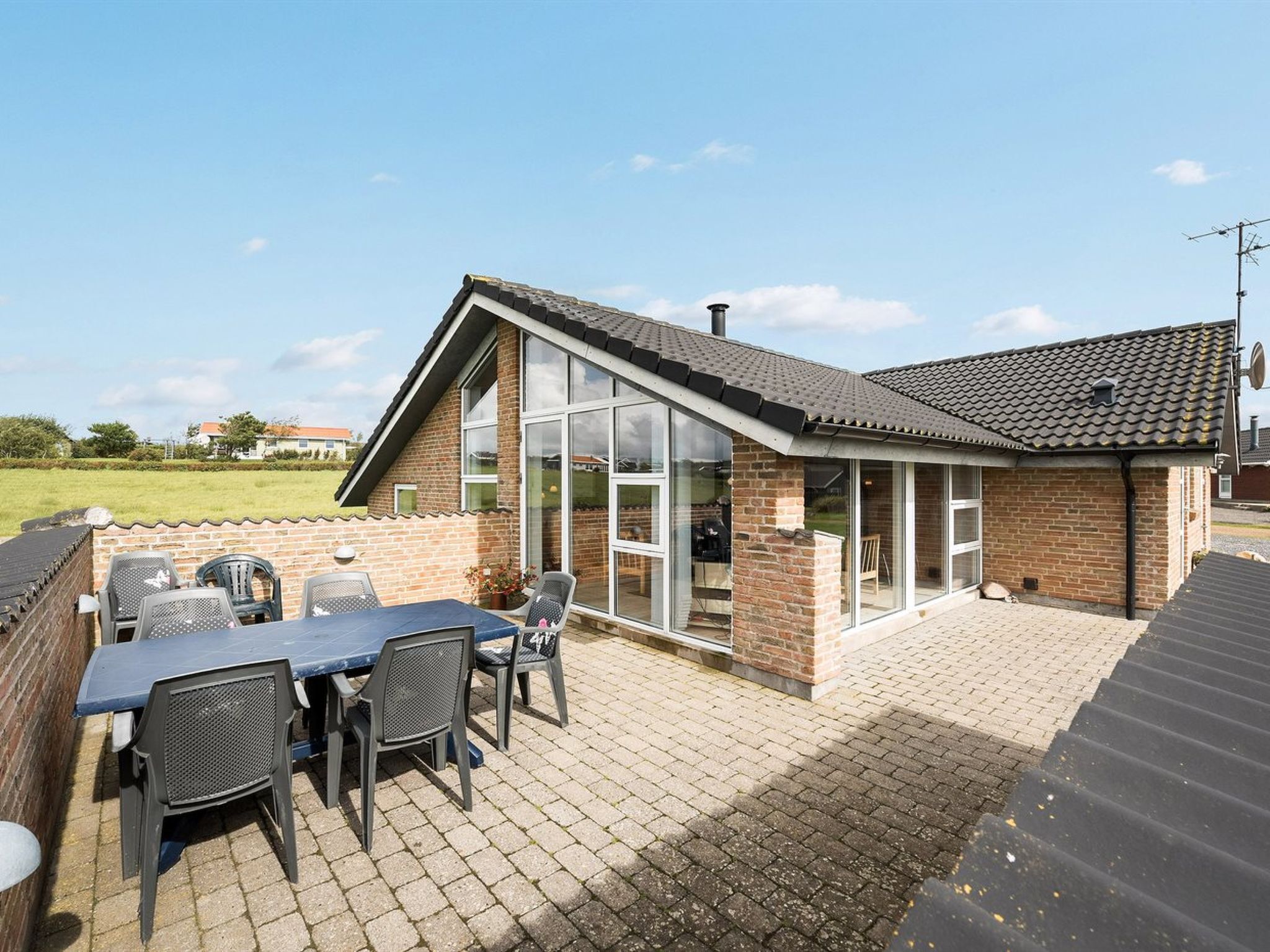 Ein modernes Haus mit Terrasse, ausgestattet mit Tisch und Stühlen, großen Fenstern und einer Ziegel-Fassade.
