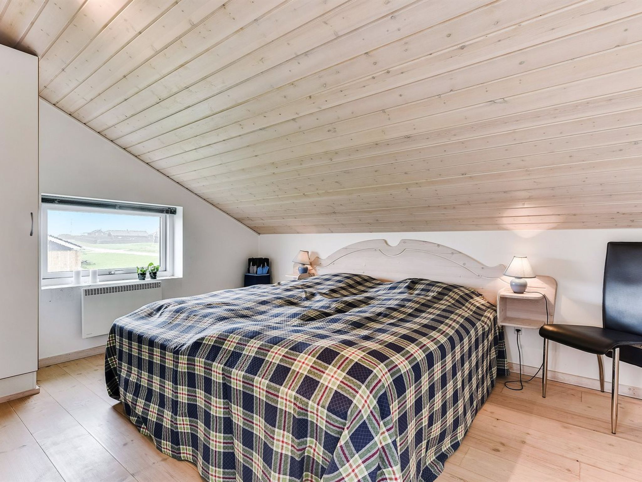 Une chambre avec un grand lit, une fenêtre donnant sur un beau paysage, une table de chevet et une chaise.