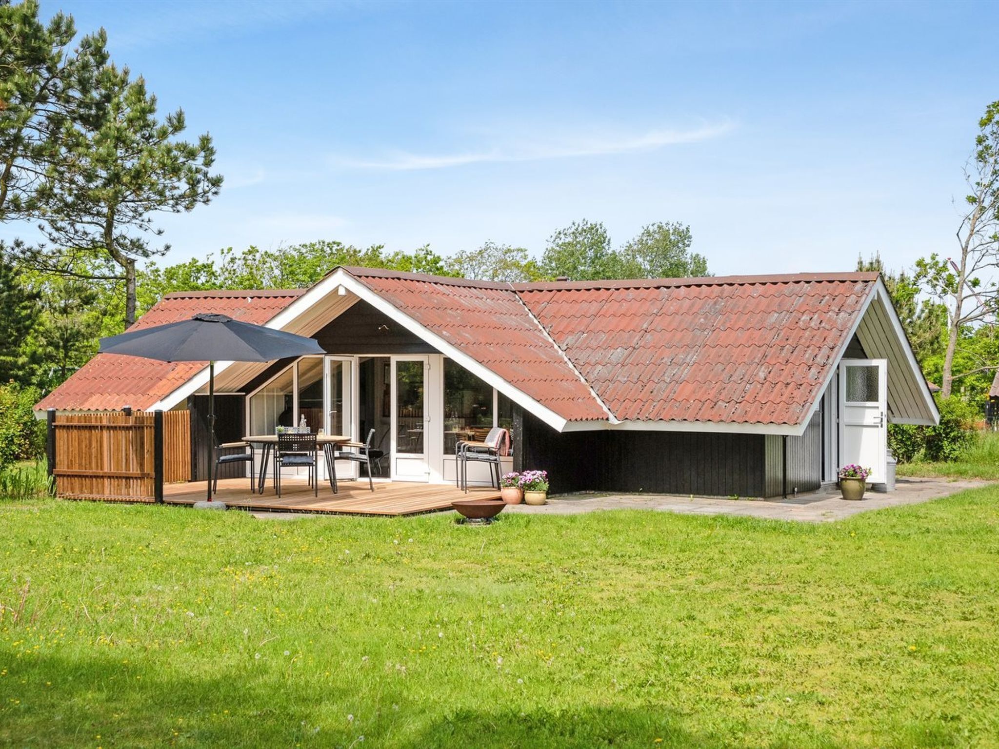 A house with a sloped roof, a patio with outdoor furniture, and a fenced yard.
