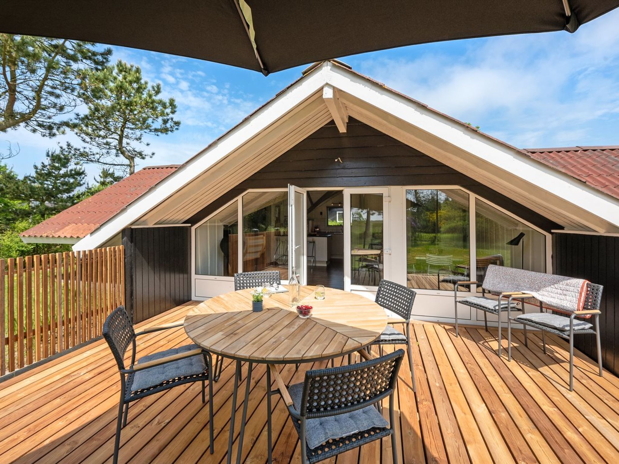 A covered deck with a table and chairs, a wooden fence, and a view of a house with a sloped roof.