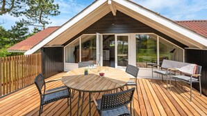A covered deck with a table and chairs, a wooden fence, and a view of a house with a sloped roof.