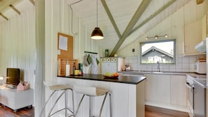 A kitchen with a central island, bar stools, a hanging light fixture, and a window overlooking a house.