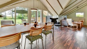 A spacious dining area with a high ceiling and large windows, wooden furniture, and a view of the outdoors.