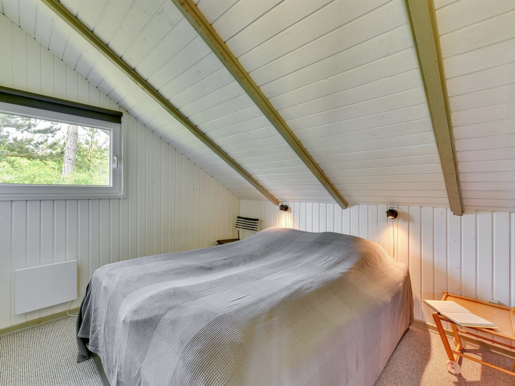 Ein Schlafzimmer mit einem Bett, einem Fenster und einer Holzbalkendecke.