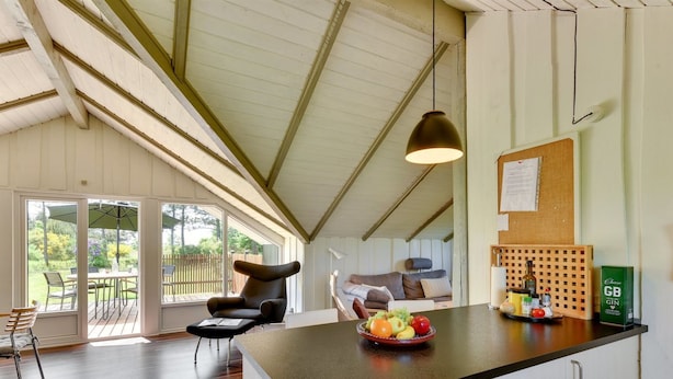 A modern kitchen with a large island, a dining area with a table and chairs, and a view of the outdoors through large windows.