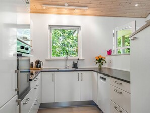 Eine moderne Küche mit weißen Schränken, einem Fenster mit Blick auf Grünflächen und einer Holzbalkendecke.