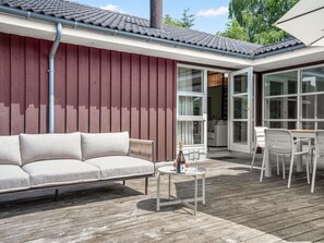 Ein moderner Außenbereich mit einer Couch, einem Tisch mit Flasche und Gläsern sowie einer Terrasse mit Blick ins Innere.