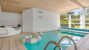 A modern indoor pool with a wooden ceiling, a jacuzzi, and a view of greenery outside.