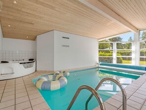 Ein moderner Innenpool mit Holzboden, einer Whirlwanne und Blick ins Grüne.