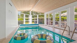 An indoor swimming pool with clear glass walls, a wooden ceiling, and two inflatable rings. - "Börje" - 600m from the sea by Interhome (Væggerløse)