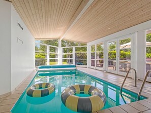 Una piscina interna con pareti in vetro trasparente, un soffitto in legno e due cerchi gonfiabili.