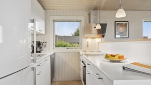 Moderni keittiö, jossa on valkoiset kaapit, ikkuna ja hedelmäkulho työtasolla.