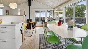 Moderni keittiö, jossa on keskeinen saareke, ruokailutila vihreine tuoleineen sekä suuret ikkunat, joista avautuu näkymä ulos.