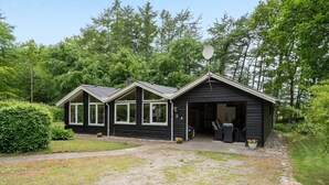 Una cabana negra amb dues habitacions annexes, una zona d'estar a l'exterior coberta i un accés de grava.