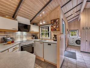 Cocina compacta con estufa, horno, pileta y lavavajillas. Hay una ventana con vista a follaje exterior.