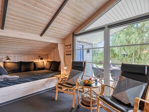 Interior acogedor de una cabaña con techo de madera, un sofá, dos sillones, una mesa con frutas y velas, y vistas a zonas verdes.