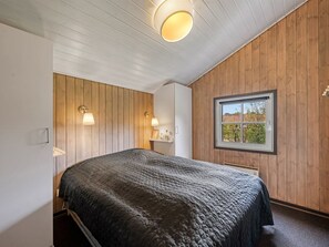 Un dormitorio con una cama, paredes de madera, un ventanal y dos lámparas fijadas a la pared.