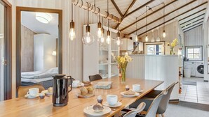 Un comedor moderno con una mesa de madera dispuesta para el desayuno, una cafetera y vistas a la cocina.