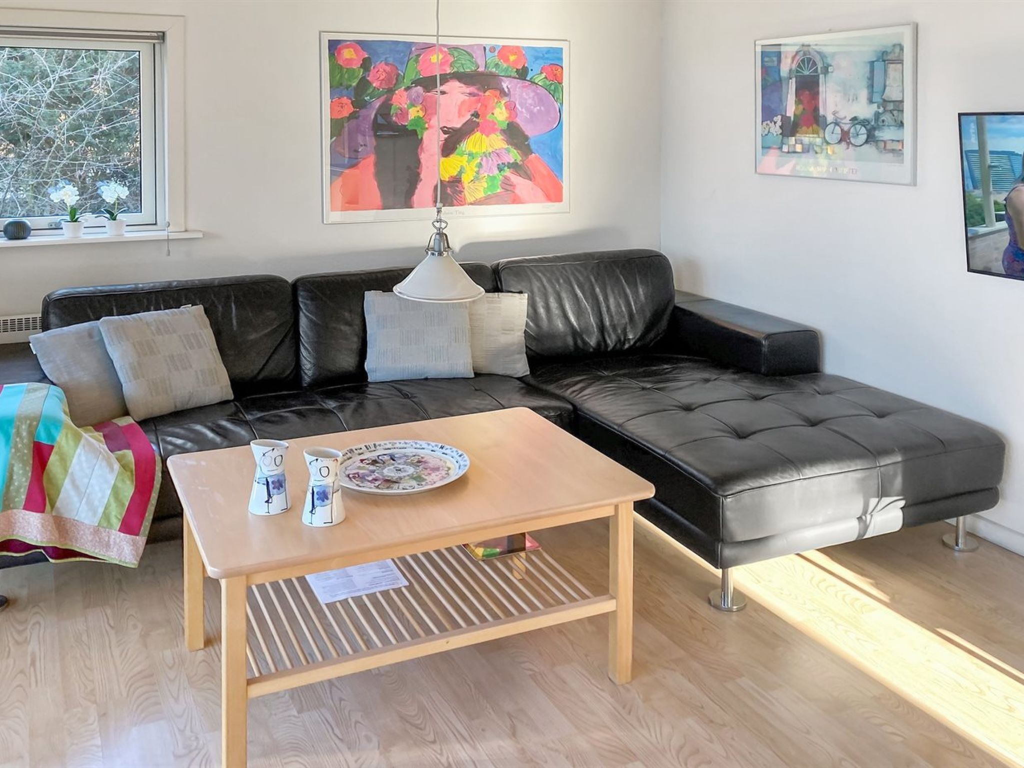 Un salon avec un canapé en cuir noir, une table basse en bois et un tableau accroché au mur.