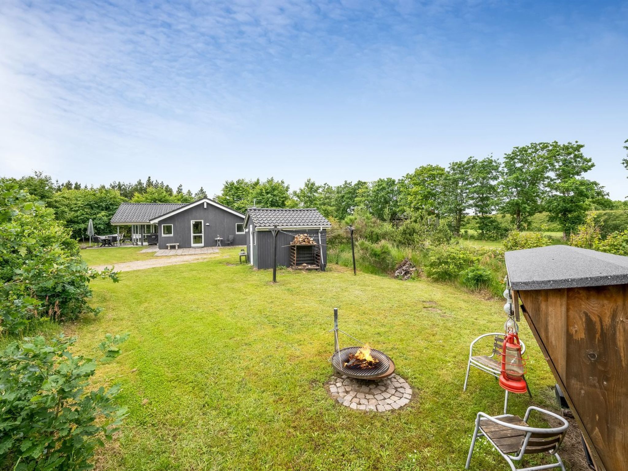 A residential area with a grassy yard, a barbecue pit, and two houses with grey roofs.