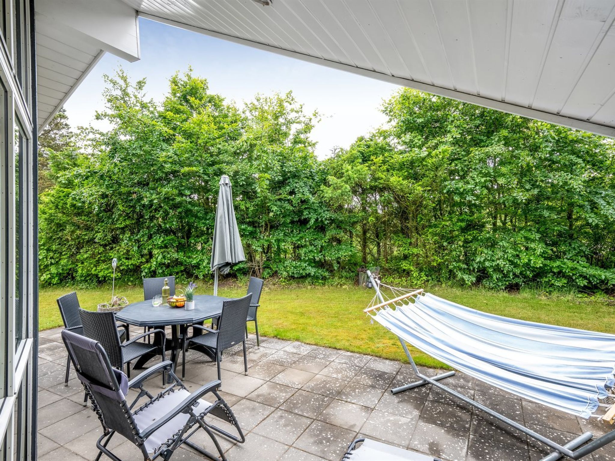 Une terrasse avec une table ronde et des chaises, un hamac et un espace abrité offrant une vue sur un jardin luxuriant.