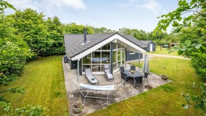 Une maison moderne dotée d’un patio comprenant une table et des chaises, un hamac et un espace salon abrité.