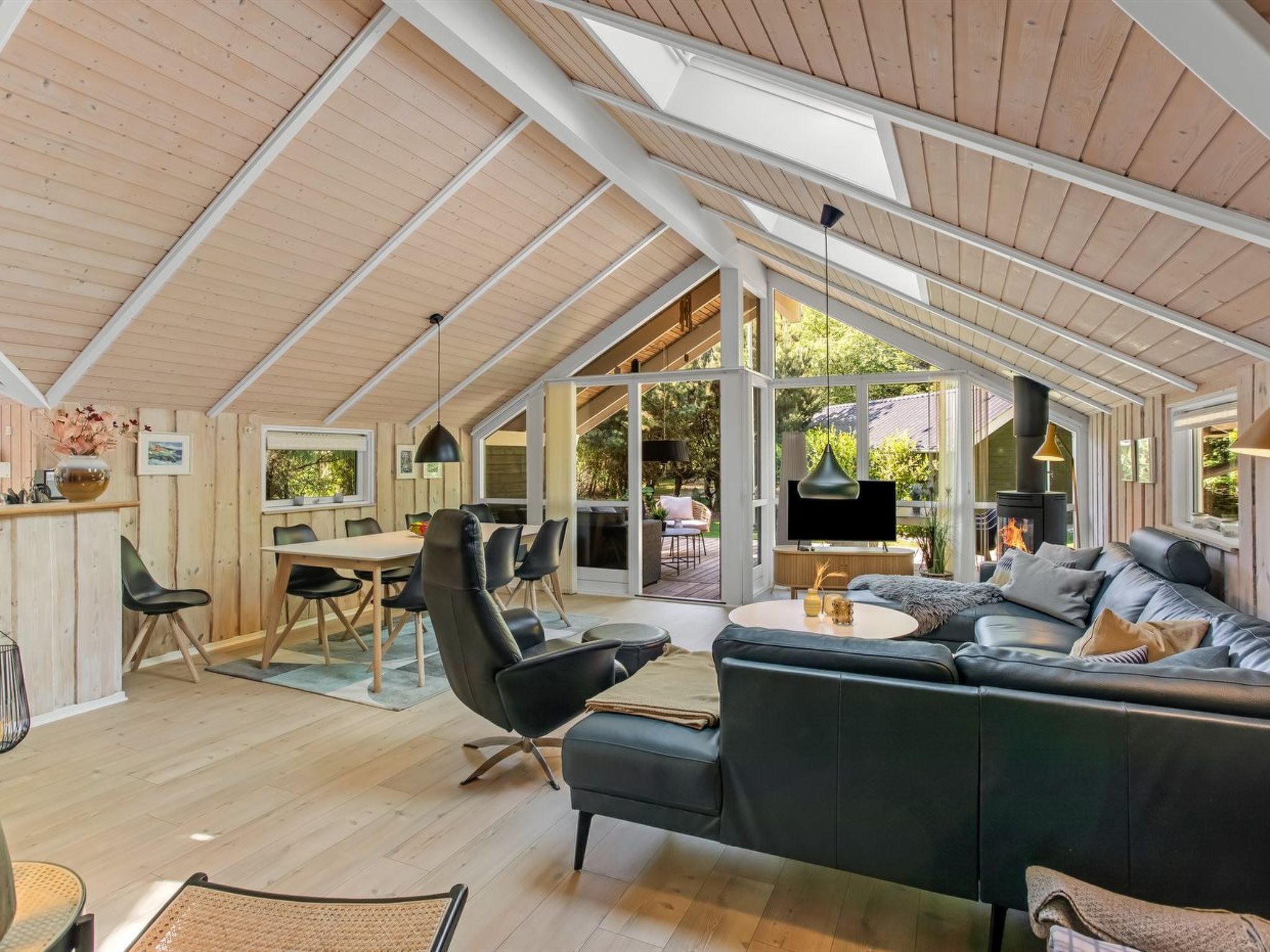 A spacious living area with a large sofa, a dining table, and chairs. There is a fireplace and a television.