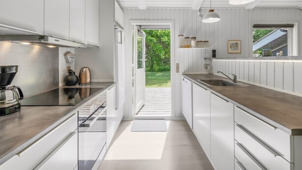 Een moderne keuken met witte kasten, een roestvrijstalen spoelbak en een raam met uitzicht op een tuin.