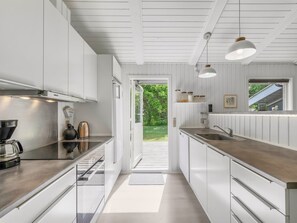 Una cocina moderna con armarios blancos, un lavamanos de acero inoxidable y una ventana con vistas a un jardín.