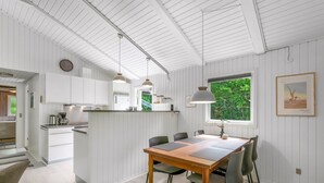 Een moderne keuken met witte kasten, een eethoek met een houten tafel en stoelen, en een groot raam met uitzicht op groen.