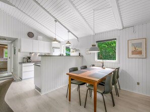 Une cuisine moderne avec des meubles blancs, un coin repas doté d’une table et de chaises en bois, et une grande fenêtre offrant une vue sur la verdure.