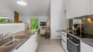 Een moderne keuken met witte kasten, roestvrijstalen apparatuur en een groot raam met uitzicht op groen.