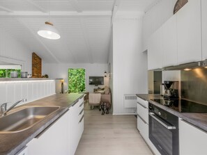 Une cuisine moderne avec des meubles blancs, des appareils en acier inoxydable et une grande fenêtre donnant sur un paysage verdoyant.